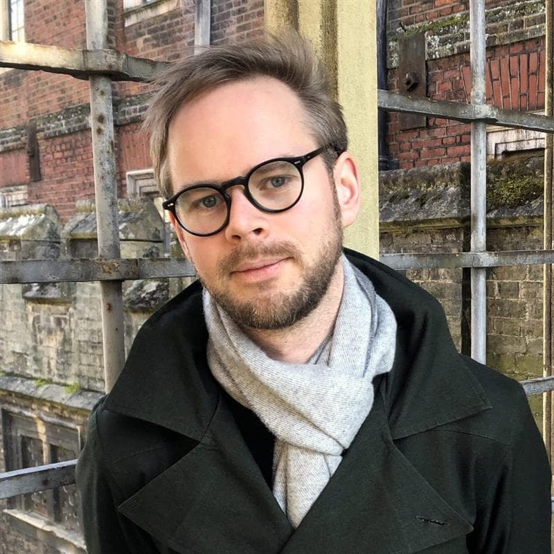 Mann med briller og svart frakk.