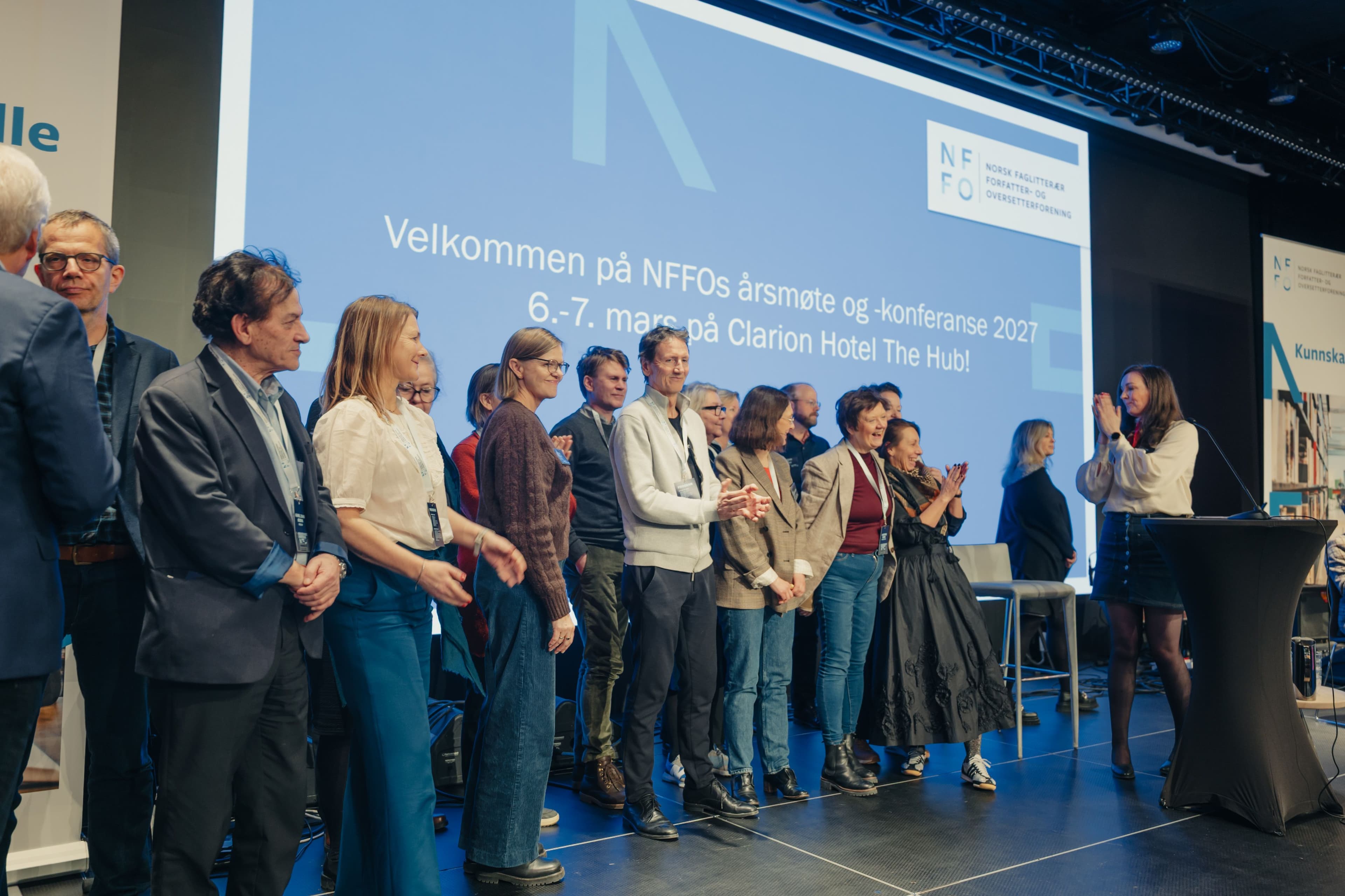 Kvinne på scene foran bakteppe hvor det står "Velkommen på NFFOs årsmøte og -konferanse 2026 14.-15. mars på Clarion Hotel The Hub!"